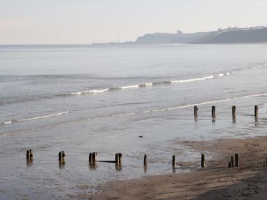 A sandy beach with wooden posts in the water and a distant coastline at The Cottage in Sandsend