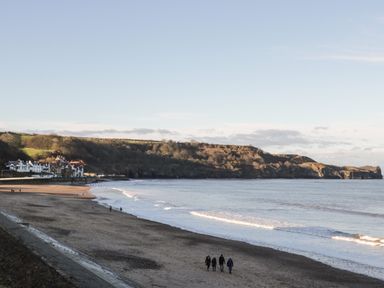 A beach with a few people walking near the shoreline and houses by the coast at The Cottage in Sandsend