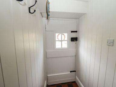 A white wooden door with a small window and black latch in a narrow hallway with white panelled walls at The Cottage in Sandsend