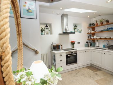 A kitchen with white cabinets open shelves with dishes a stove and a sink at The Cottage in Sandsend
