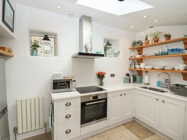A kitchen with white cabinets wooden shelves and modern appliances at The Cottage in Sandsend