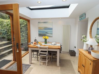 A dining area with a wooden table and six chairs next to large glass doors and a skylight at The Cottage in Sandsend