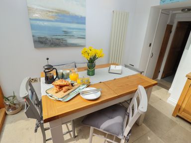 A dining table with a vase of yellow flowers croissants juice and coffee in a kitchen at The Cottage in Sandsend