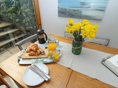 A wooden dining table set with a tray of croissants a French press a jug and glasses of orange juice and a vase of yellow flowers at The Cottage in Sandsend