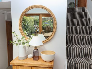 Hallway with wooden table holding a lamp vase and bowl next to striped carpeted stairs at The Cottage in Sandsend