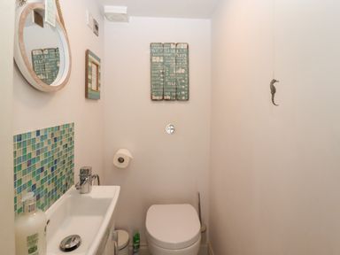 A small bathroom with a toilet a sink a round mirror and wall decorations at The Cottage in Sandsend