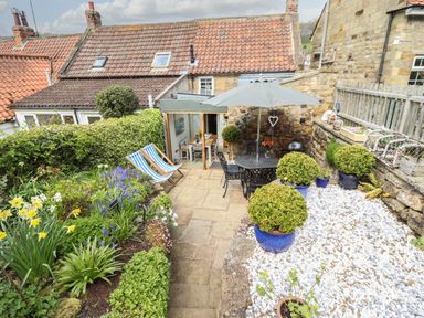 A garden with plants flowers lounge chairs and a patio table with umbrella at The Cottage in Sandsend