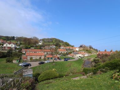 A village with houses along a river and parked cars on a road with trees on a hill at The Cottage in Sandsend