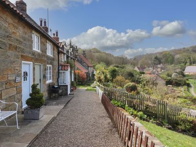 A gravel pathway beside stone cottages with potted plants and a wooden fence along a garden at The Cottage in Sandsend