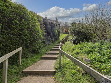 An outdoor pathway with steps and wooden handrails surrounded by shrubs and greenery at The Cottage in Sandsend