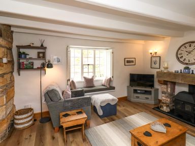 A living room with a gray armchair ottoman and wooden tables a TV on a corner cabinet and a fireplace at The Cottage in Sandsend