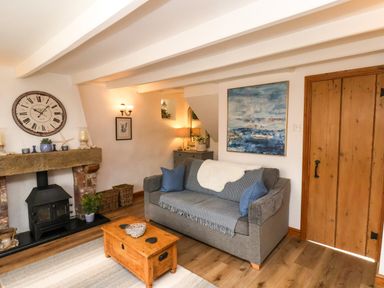 A living room with a gray sofa and blue cushions a wooden coffee table and a wood burning stove at The Cottage in Sandsend