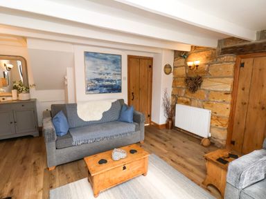 A living room with a gray sofa and wooden bookshelf a wooden chest and a stone wall at The Cottage in Sandsend