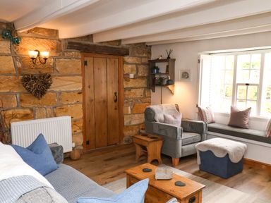 A living room with wooden door stone wall armchair window seat and coffee table at The Cottage in Sandsend