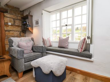 A sitting area with a grey armchair a window seat with cushions and a footstool at The Cottage in Sandsend