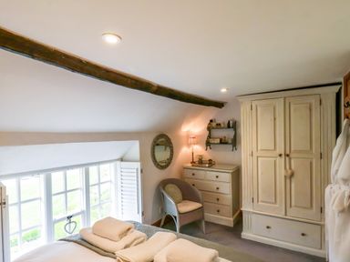 A bedroom with a bed, dresser, wardrobe, chair, and windows with shutters at The Cottage in Sandsend