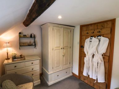 A corner of a bedroom with a wooden wardrobe a chest of drawers a chair and bathrobes hanging on a wooden door at The Cottage in Sandsend