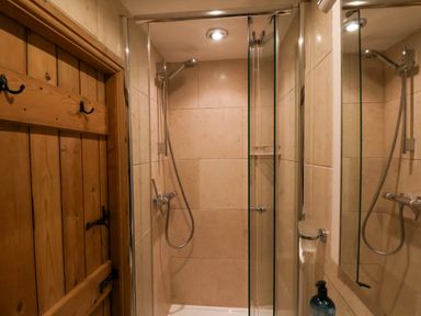 A bathroom shower area with a glass door wooden door and wall mounted shower fixtures at The Cottage in Sandsend