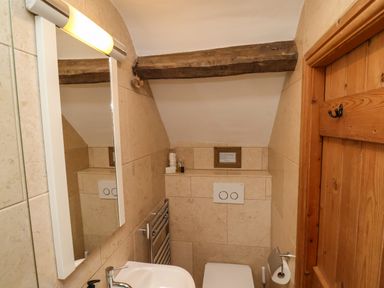 A small bathroom with a sink, mirror, toilet, wooden door, and exposed wooden beam at The Cottage in Sandsend