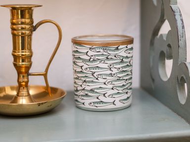 A brass candle holder and a container with fish pattern on a shelf at The Cottage in Sandsend