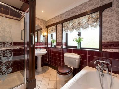 A bathroom with a shower enclosure a pedestal sink a toilet with wooden seat a bathtub and floral curtains at Seawinds in Robin Hoods Bay