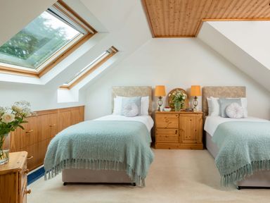 A bedroom with two single beds a wooden cabinet two table lamps and slanted windows at Seawinds Robin Hood'S Bay