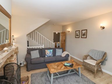 A living room with a gray sofa and wicker chair near a wooden coffee table and fireplace at Rooftops Cottage in Whitby