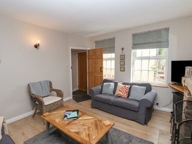 A living room with a gray sofa, a wicker chair, a wooden coffee table, and windows with gray blinds at Rooftops Cottage in Whitby