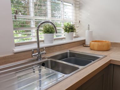 A kitchen sink with chrome faucet near a window with blinds and potted plants on the windowsill at Rooftops Cottage in Whitby