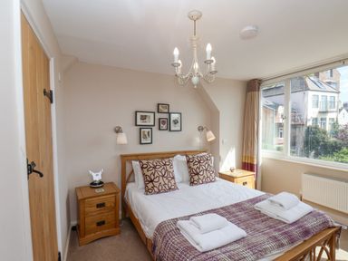 A bedroom with a double bed two bedside tables a chandelier and a window showing houses outside at Rooftops Cottage in Whitby