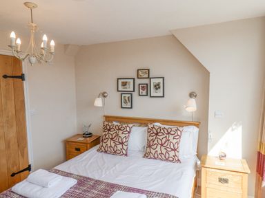 A bedroom with a double bed, patterned pillows, bedside tables, lamps, and framed pictures on the wall at Rooftops Cottage in Whitby