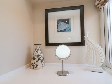 A corner with a decorative vase a round mirror and a leaf sculpture under a framed picture at Rooftops Cottage in Whitby