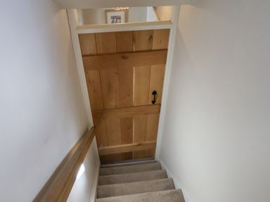 A staircase with carpeted steps leading to a wooden door with a black handle at Rooftops Cottage in Whitby