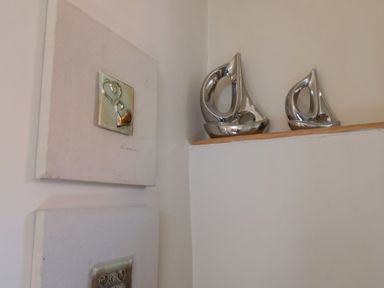 Two silver sailboat ornaments on a wooden ledge in a corner with two square artworks on the adjacent wall at Rooftops Cottage in Whitby