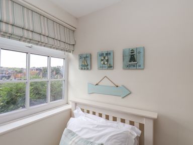 A bedroom corner with a white bed frame and pillow under a window with striped blinds and nautical wall art at Rooftops Cottage in Whitby