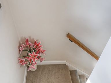 A staircase with beige carpet a wooden handrail and a vase with pink flowers at Rooftops Cottage in Whitby