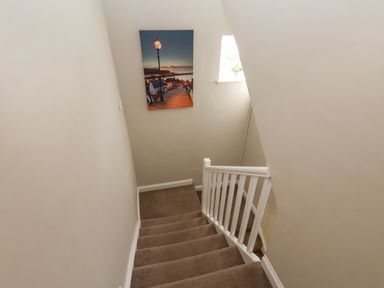 A carpeted staircase with a white railing and a window with a plant and a wall picture at Rooftops Cottage in Whitby
