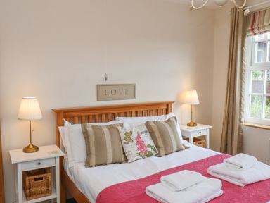 A bedroom with a wooden bed frame white bedding and three pillows two bedside tables with lamps and a window at Rooftops Cottage in Whitby