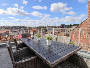 A rooftop patio with a table, chairs, potted plants, and a view of buildings and rooftops at Rooftops Cottage in Whitby