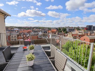 A rooftop terrace with a table and chairs overlooking rooftops and buildings at Rooftops Cottage in Whitby