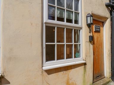 A window with white frames next to a wooden door with a light and sign reading Rooftops Cottage in Whitby