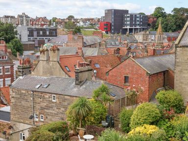 A view of rooftops with brick and stone buildings and a garden with trees and bushes at Rooftops Cottage in Whitby