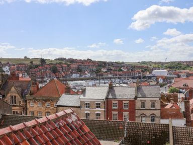 View of red and gray rooftops with buildings and a marina in the background at Rooftops Cottage in Whitby