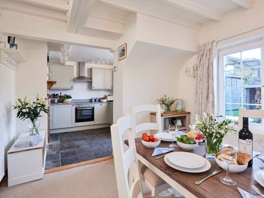 A dining table set with plates bowls and wine in a room with a kitchen in the background at Rigg Cottage Sandsend