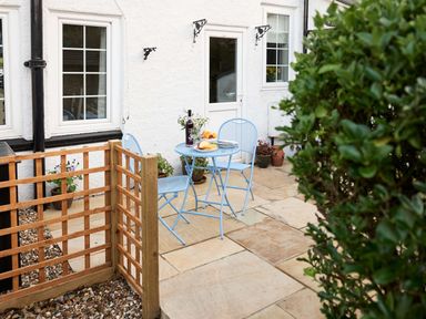 An outdoor patio with a blue table and chairs set near a white house with windows and a door at Rigg Cottage in Sandsend