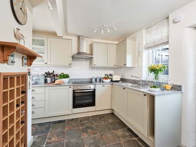 A kitchen with beige cabinets a stainless steel oven and extractor a granite countertop and slatestone floor at Rigg Cottage in Sandsend