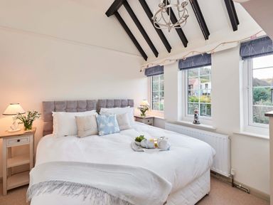 A bedroom with a bed between two nightstands with lamps and three windows with blue blinds at Rigg Cottage in Sandsend
