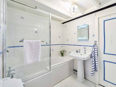 A bathroom with a bathtub, pedestal sink, mirror, towel rails, and white tiles with blue nautical motifs at Rigg Cottage in Sandsend