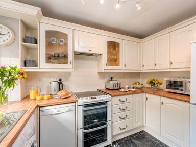 A kitchen with white cabinets a stove a dishwasher a washing machine a microwave a toaster a kettle flowers and orange juice at Esk View Cottage in Grosmont