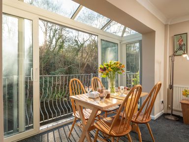 A dining area with a wooden table and four chairs next to glass doors overlooking trees at Esk View Cottage in Grosmont